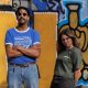 Vor einer gelb-blauen Graffitiwand stehen Natalie und Greg von Press Club. Natalie hält lässig zurückgelehnt die Hände hinterm Rücken und Greg trägt eine Sonnenbrille.